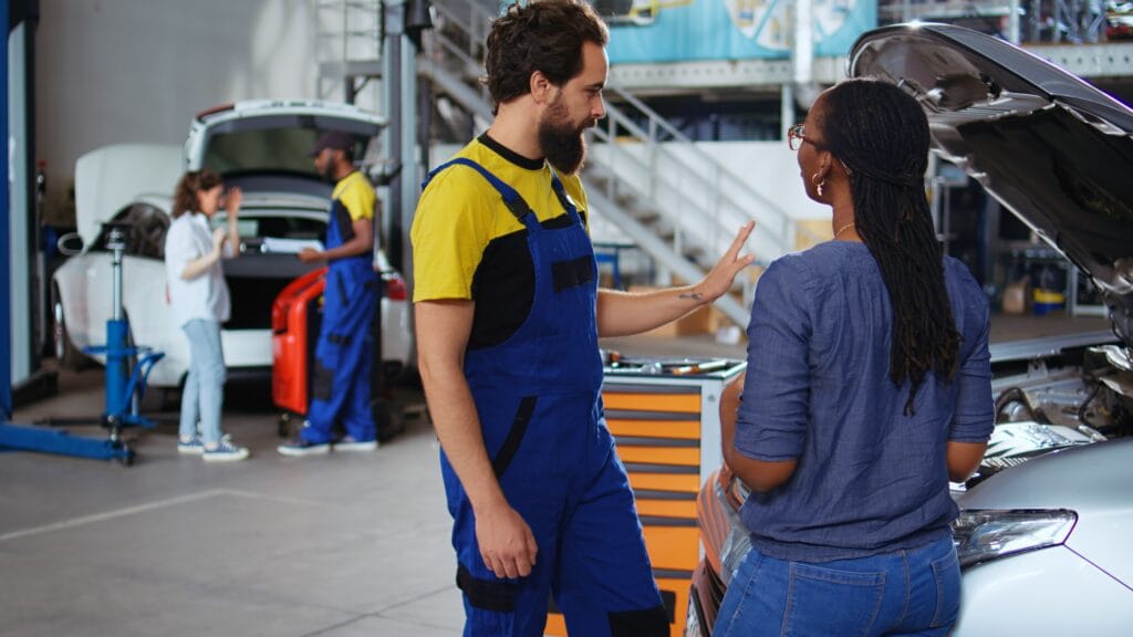 Teamworking colleagues in garage workspace fixing car for customers, thoroughly checking underneath vehicle hood. Mechanics doing routine maintenance on automobile in auto repair shop